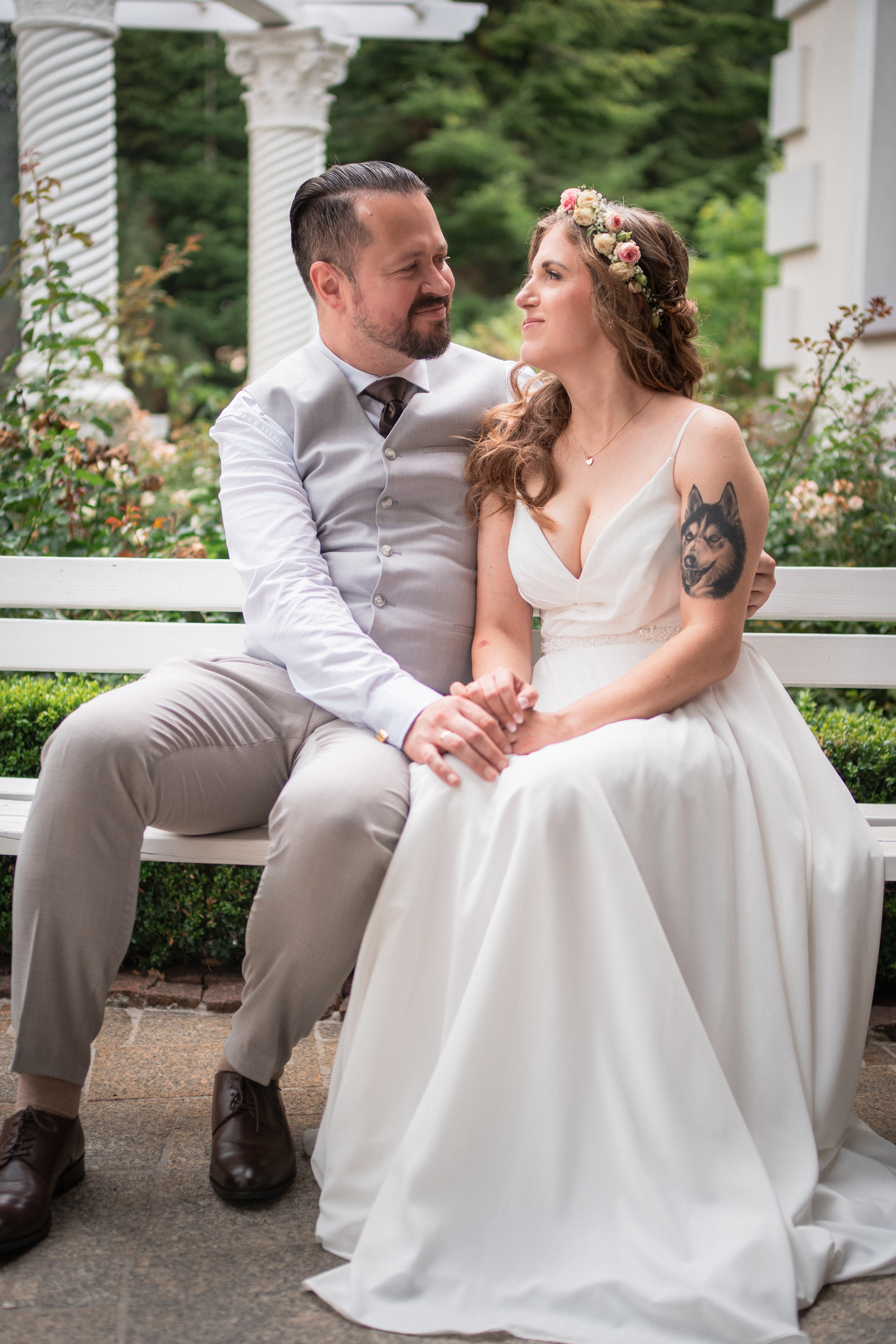 Para młoda siedząca na ławce w ogrodzie, uśmiechnięta i zapatrzona w siebie.