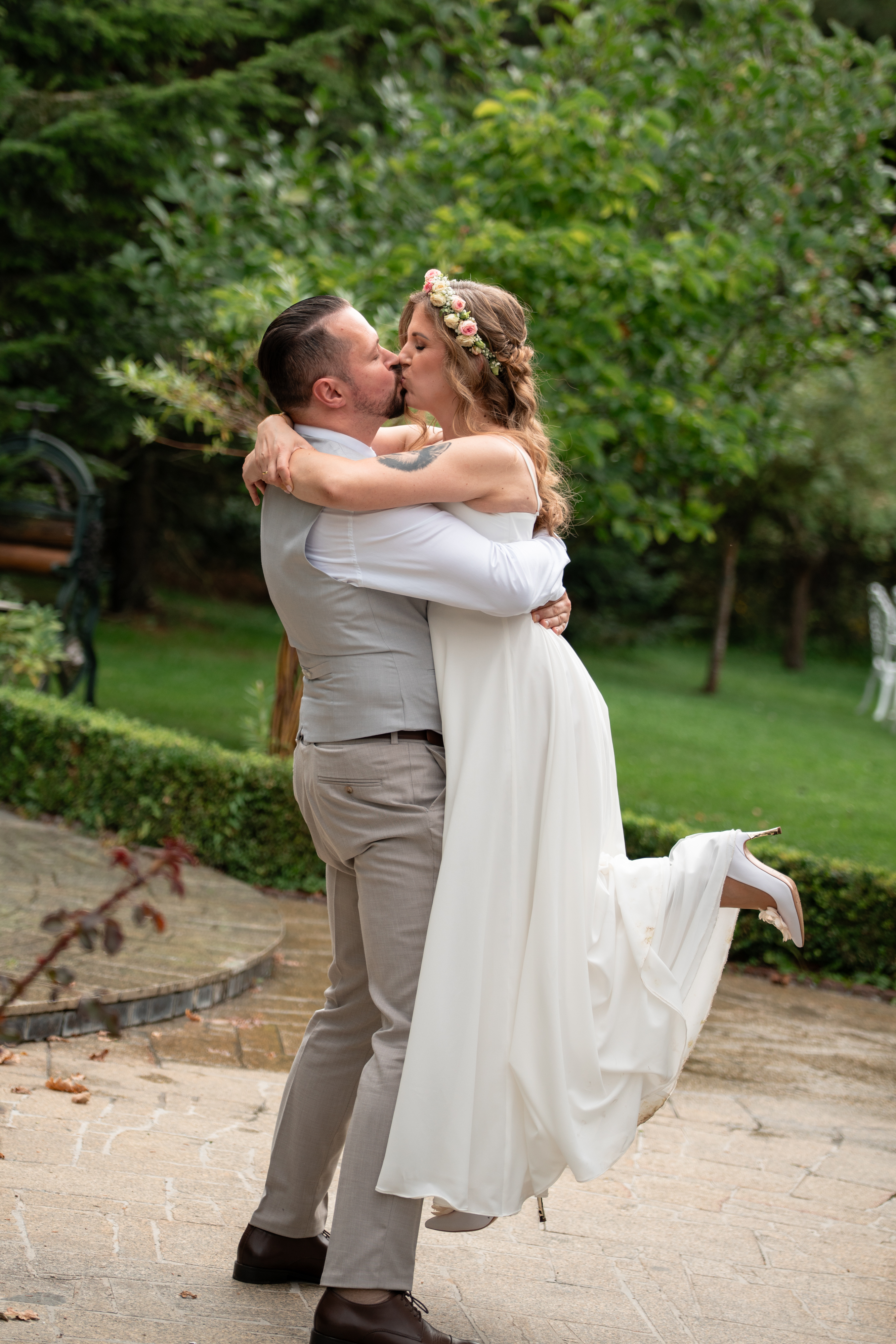 Pan młody unosi pannę młodą w objęciach podczas pocałunku w ogrodzie.