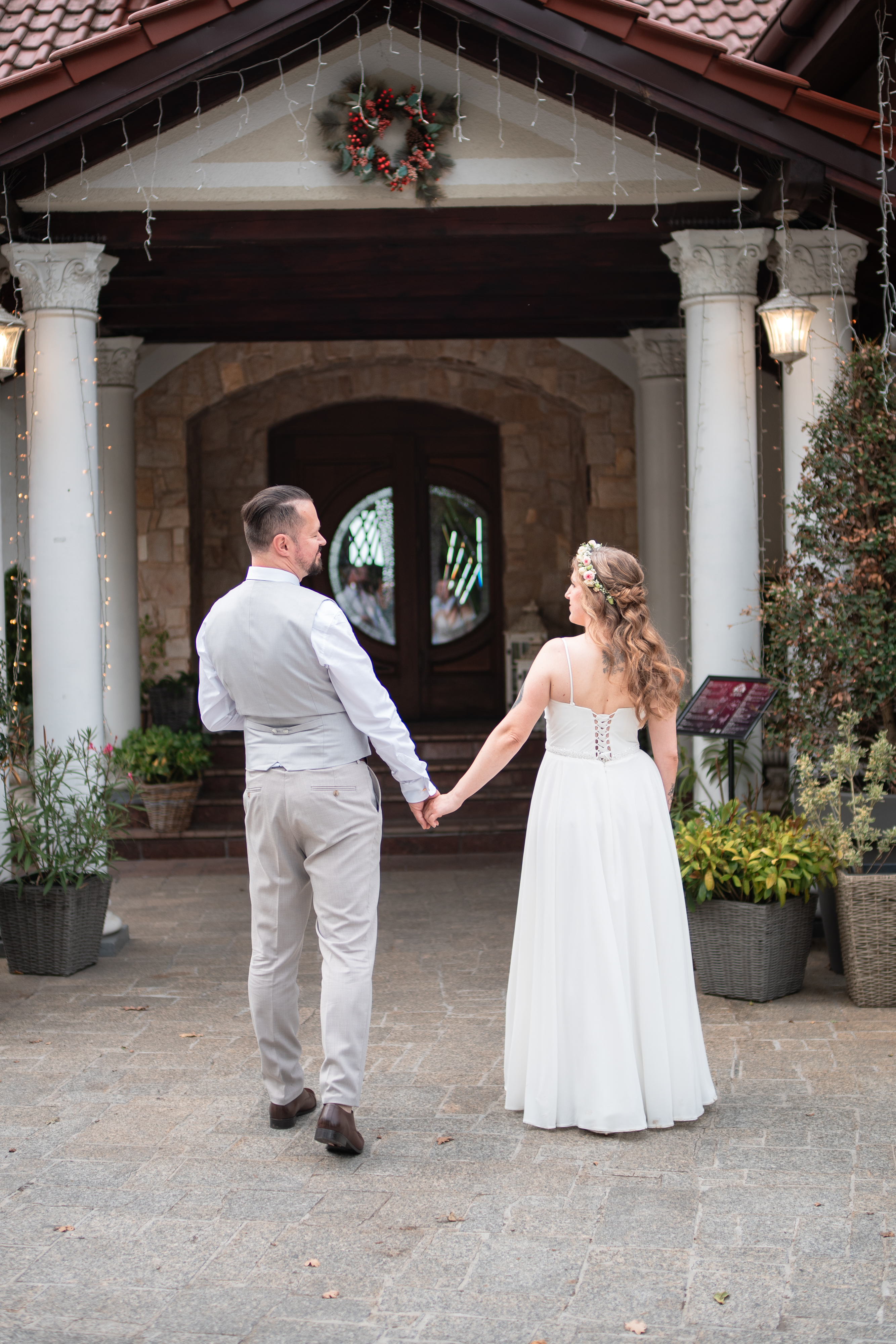 Para młoda trzymająca się za ręce wchodzi do eleganckiego dworku weselnego.